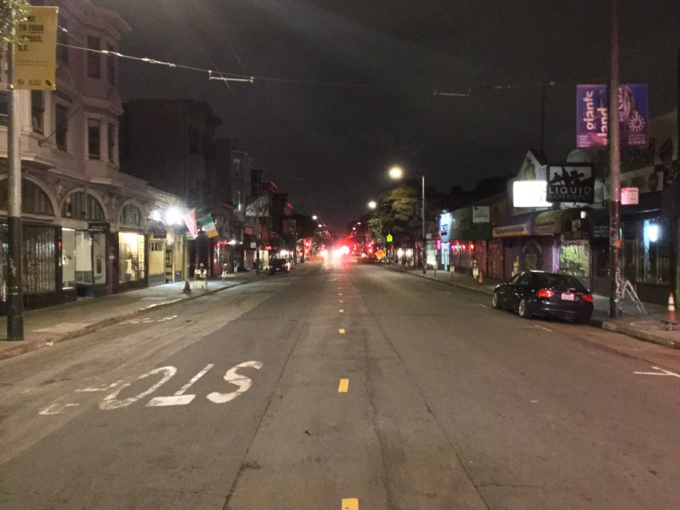 Looking down Haight Street at night, with only a couple of parked cars, and one more on the street with headlamps in the distance, with no one on the sidewalks.